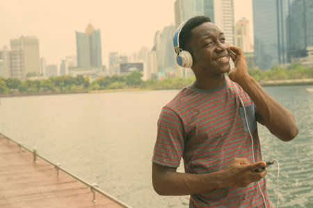 Happy young handsome African man listening to music at the parkの写真素材