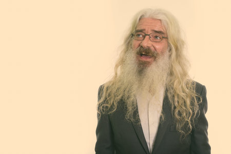 Studio shot of happy senior bearded businessman smiling while thinking and wearing eyeglasses