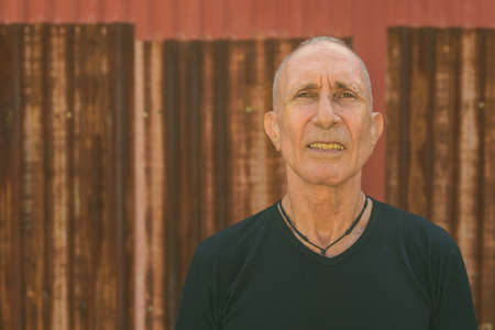 Close up of happy bald senior man smiling against old rusty sheet wallの写真素材
