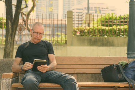 Bald senior tourist man using digital tablet at the parkの写真素材