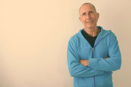 Studio shot of happy bald senior man smiling with arms crossed against white backgroundの写真素材