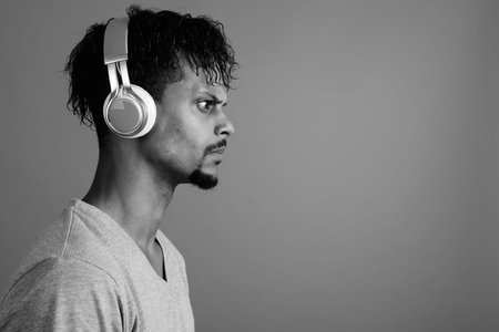 Young bearded handsome African man listening to music against gray background