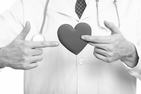 Studio shot of mature man doctor holding heart and pointing finger