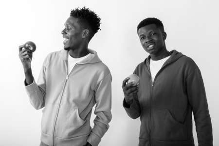 Two happy young African friends together holding apples against white backgroundの写真素材