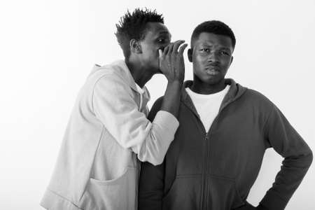 Studio shot of young slim black African man whispering to young black African man while thinkingの写真素材