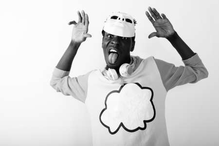 Studio shot of young black African man sticking tongue out while wearing white mask on top of headの写真素材