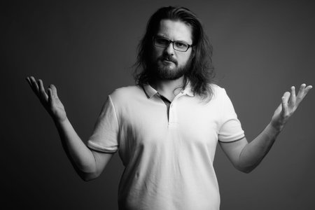 Young bearded man wearing white polo shirt against gray background