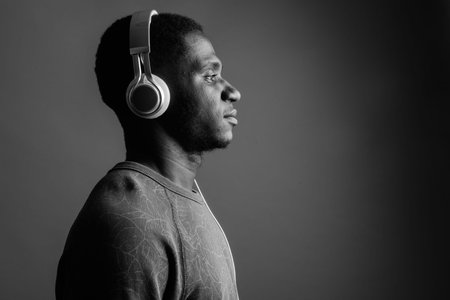 Young African man listening to music against gray background