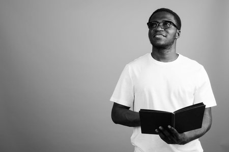 Young African man wearing white shirt and eyeglasses against gray background