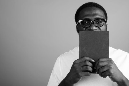 Young African man wearing white shirt and eyeglasses against gray background