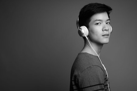 Young handsome Asian man listening to music against gray background
