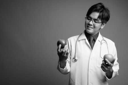 Young handsome Asian man doctor wearing eyeglasses against gray backgroundの写真素材