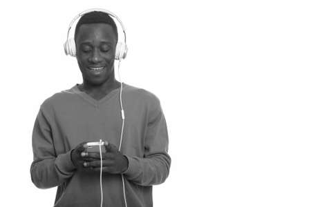 Young happy African man smiling and using mobile phone while listening to musicの写真素材