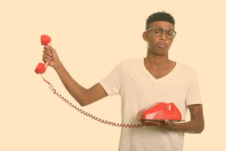 Young handsome African man looking annoyed while holding telephoneの写真素材