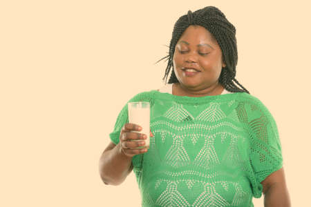 Studio shot of happy fat black African woman smiling while holding and looking at glass of milkの写真素材