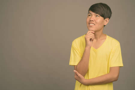 Young Asian teenage boy against gray backgroundの写真素材