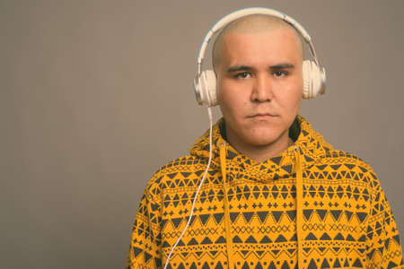 Young bald Asian man listening to music against gray backgroundの写真素材