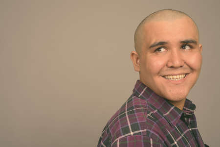 Young bald Asian businessman against gray backgroundの写真素材