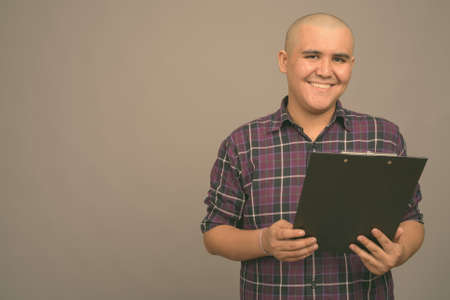 Young bald Asian businessman against gray backgroundの写真素材