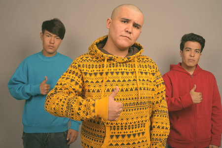 Three young Asian men wearing warm clothing against gray background