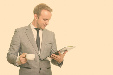 Handsome Caucasian businessman reading clipboard while drinking coffee
