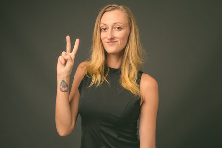 Young beautiful businesswoman with straight blond hair against gray background