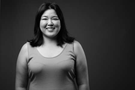 Beautiful overweight Asian woman against gray backgroundの写真素材