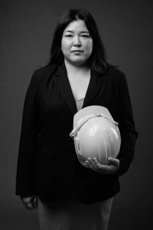 Beautiful overweight Asian businesswoman holding hardhat against gray backgroundの写真素材