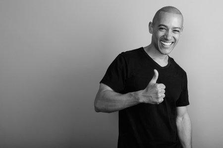 Handsome bald man wearing black shirt against gray background