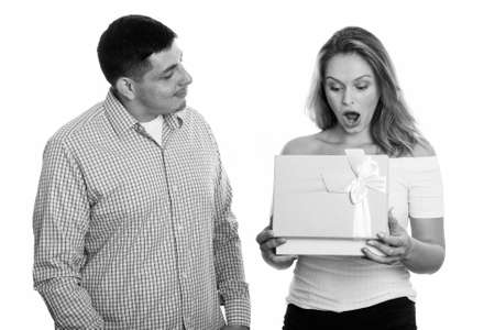 Studio shot of young couple in love with woman opening gift box looking surprisedの写真素材