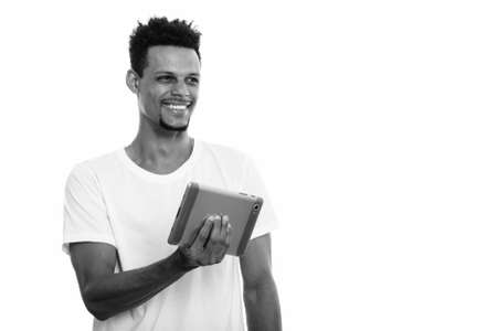 Thoughtful young happy African man smiling while holding digital tabletの写真素材