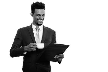 Young happy African businessman smiling while reading on clipboard and holding coffee cupの写真素材