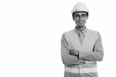 Studio shot of young happy man construction worker smiling while wearing eyeglasses with arms...
