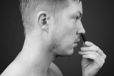 Young handsome man shirtless while grooming against gray backgroundの写真素材