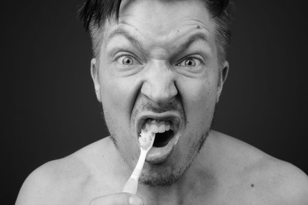 Young handsome man shirtless while grooming against gray background