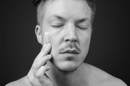 Young handsome man shirtless while grooming against gray backgroundの写真素材