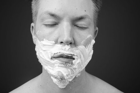 Young handsome man shirtless while grooming against gray background