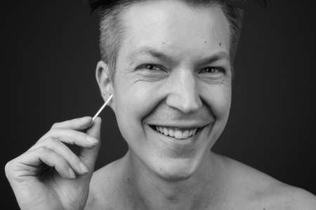Young handsome man shirtless while grooming against gray backgroundの写真素材