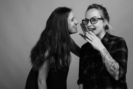 Two young beautiful woman friends against gray background