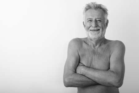 Studio shot of happy senior bearded man smiling shirtless with arms crossed against white backgroundの写真素材