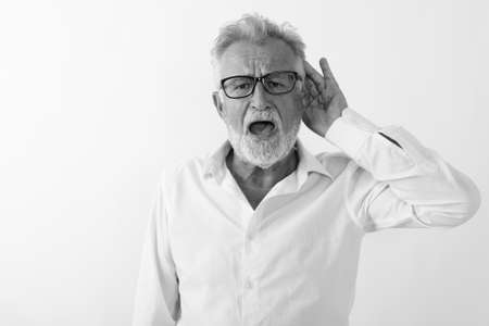 Studio shot of handsome senior bearded man listening while wearing eyeglasses against white backgroundの写真素材