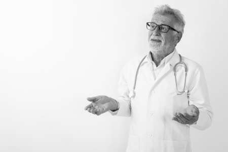Studio shot of handsome senior bearded man doctor thinking while looking confused against white backgroundの写真素材