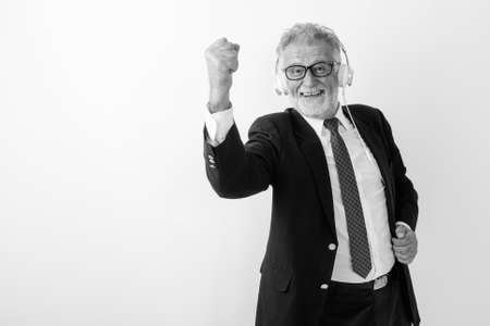 Studio shot of happy senior bearded businessman smiling while listening to music and looking motivated with eyeglasses against white backgroundの写真素材