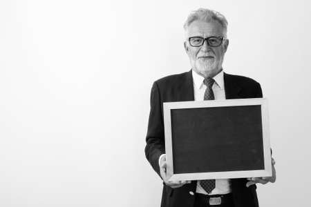 Studio shot of handsome senior bearded businessman holding blank blackboard against white backgroundの写真素材