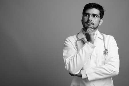 Young handsome bearded Persian man doctor against gray backgroundの写真素材