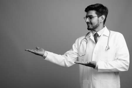 Young handsome bearded Persian man doctor against gray backgroundの写真素材