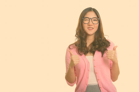 Young happy Asian woman giving thumbs up and winking