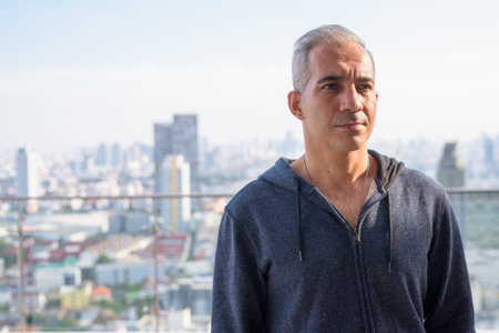 Handsome Persian man with gray hair thinking against view of the city
