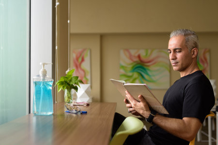 Handsome Persian man with gray hair reading book at the library