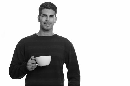 Young happy Persian man smiling and holding coffee cup